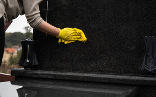 person using a soft cloth to wipe down a black granite headstone