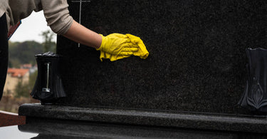 person using a soft cloth to wipe down a black granite headstone