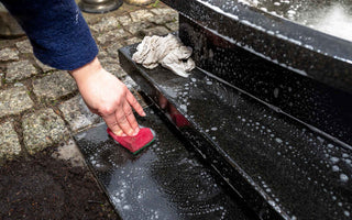 person scrubbing a black tombstone with a red sponge and soapy water