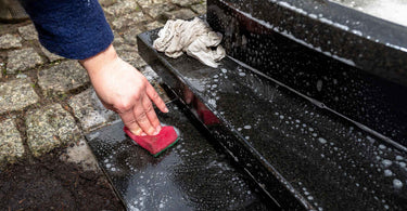 person scrubbing a black tombstone with a red sponge and soapy water