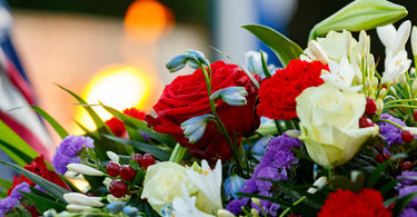 Close-up of a vibrant memorial floral arrangement, featuring red roses, white lilies, and purple flowers