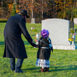 Granddaughter and grandfather walking through grass in a cemetery 