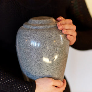 person holding a gray urn with both hands