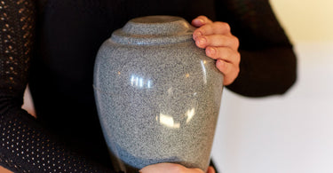 person holding a gray urn with both hands