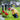 little boy in a yellow rain coat crouching in front of a headstone with flowers in front of it