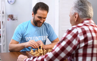 male volunteer playing chess with older man in nursing home