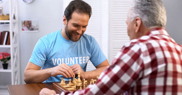 male volunteer playing chess with older man in nursing home