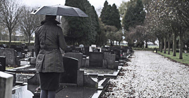 gray photo of a woman standing in front of a headstone with an umbrella