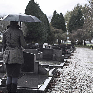 gray photo of a woman standing in front of a headstone with an umbrella