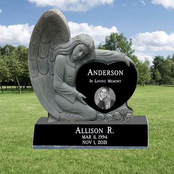 Carved Angel hugging a Single Black Granite Heart Headstone. In the heart is a last name, and the words "in loving memory", on the base is a first name, middle initial, birth and death date.