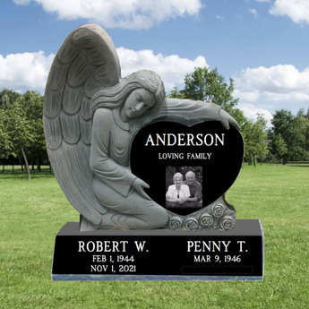 Carved Angel hugging a companion Black Granite Heart Headstone. In the heart is a last name, and the words " loving family", on the base are first names, middle initial, birth and death date.