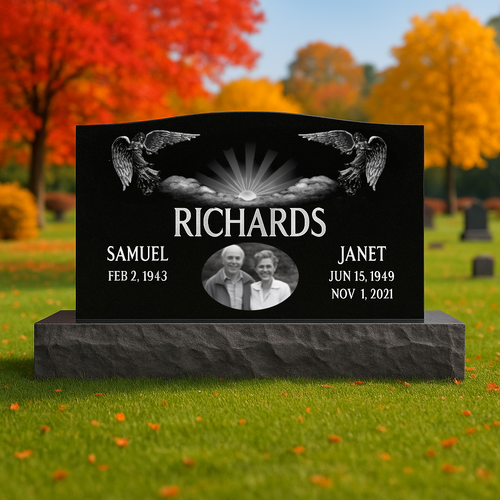 Black granite headstone with angel designs and engraved names and dates in a cemetery setting.